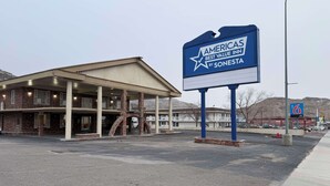 A motel with a large sign, a covered parking area, and a mountainous backdrop. - Americas Best Value Inn Wendover (Wendover)
