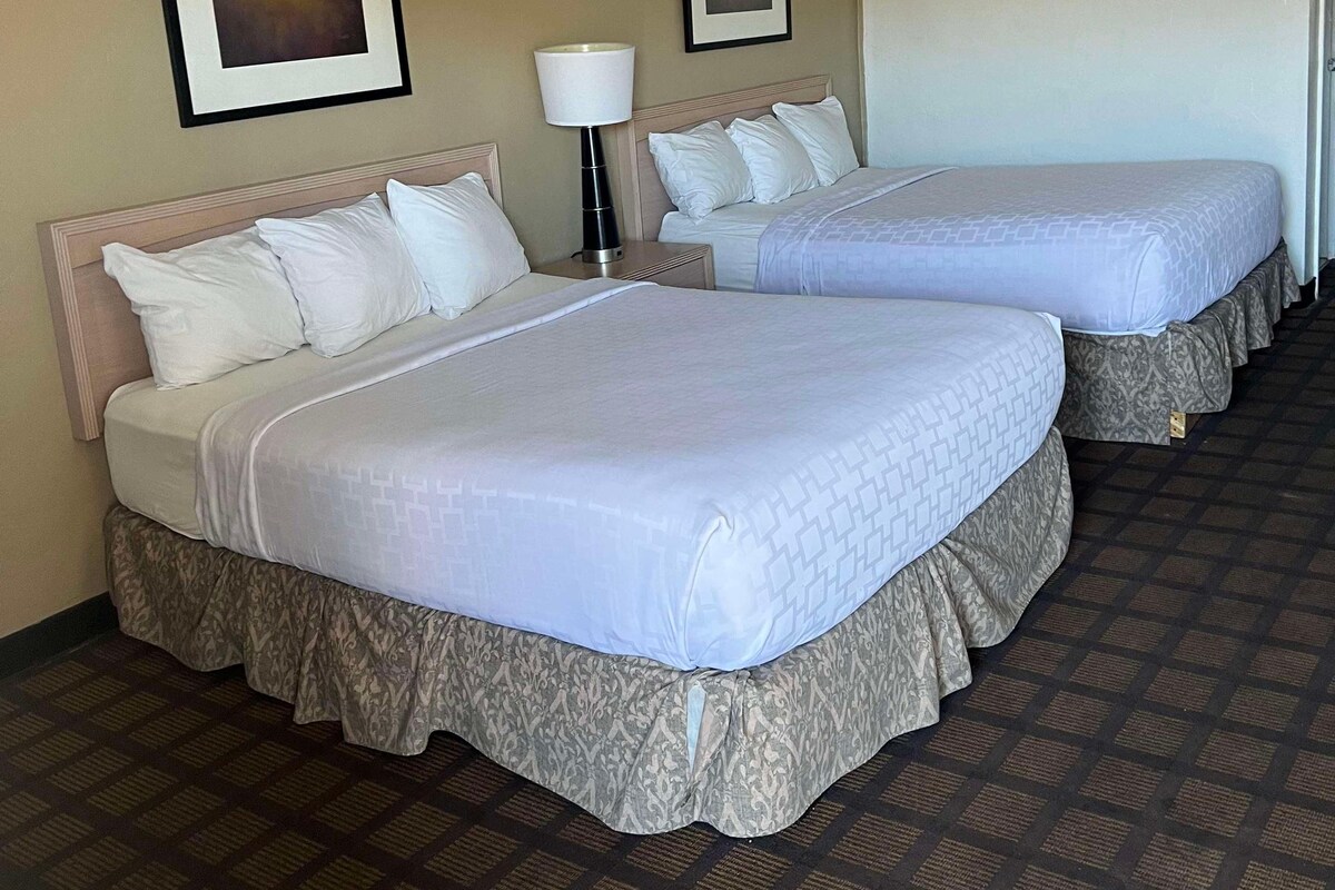A hotel room with two beds, a nightstand with a lamp, and framed pictures on the wall.
