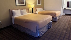 A hotel room with two beds, a nightstand, a lamp, and two framed pictures on the wall.
