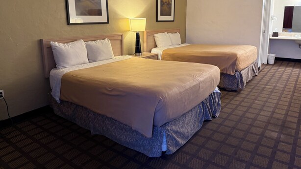 A hotel room with two beds, a nightstand, a lamp, and two framed pictures on the wall. - Americas Best Value Inn Wendover (Wendover)