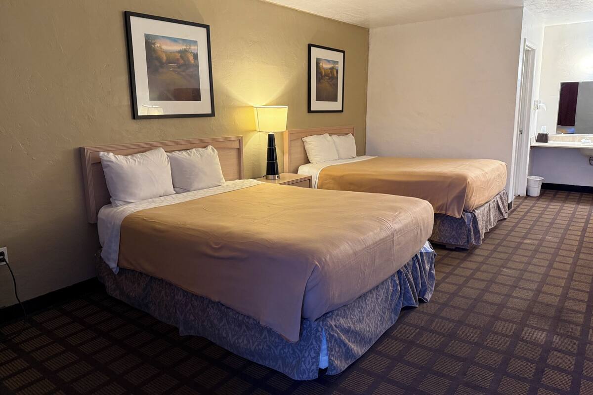 A hotel room with two beds, a nightstand, a lamp, and two framed pictures on the wall.