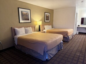 A hotel room with two beds, a nightstand, a lamp, and two framed pictures on the wall.