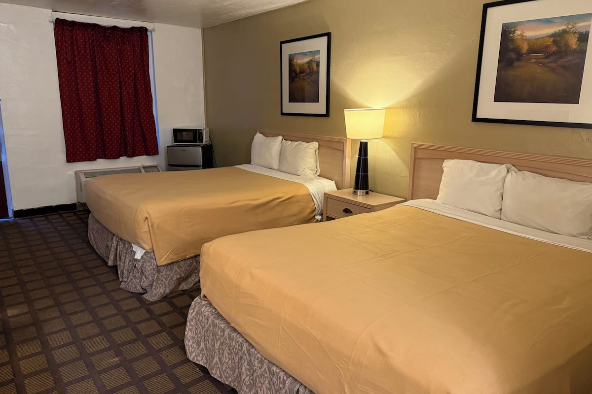 A hotel room with two beds, a microwave, a lamp, and a framed picture on the wall.