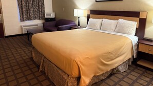 A hotel room with a large bed, a flat-screen TV, a microwave, a desk with a lamp, and a window with curtains.