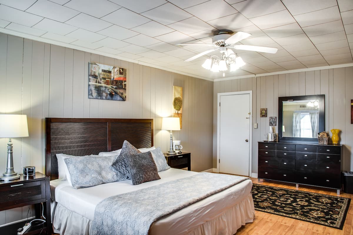 A bedroom with a large bed, a ceiling fan, a dresser, and a painting on the wall.