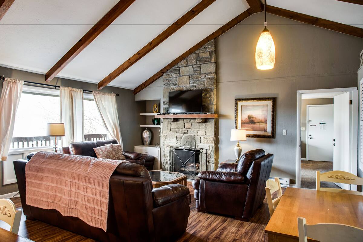A cozy living room with a stone fireplace, leather furniture, and a wooden ceiling.