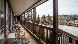 A covered outdoor area with a wooden railing, stone flooring, and metal chairs. - Cliff Dwellers Inn (Blowing Rock)