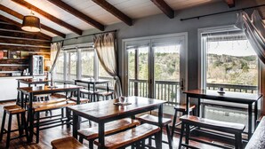 A rustic dining area with wooden tables and benches, large windows with curtains, and a view of the outdoors. - Cliff Dwellers Inn (Blowing Rock)