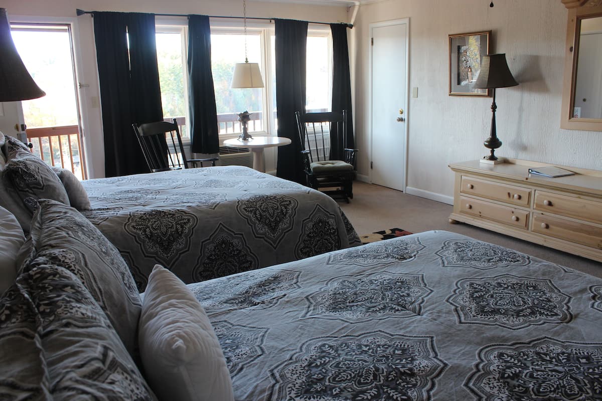 A bedroom with two beds, a dresser, a chair, a table, and a window with curtains.