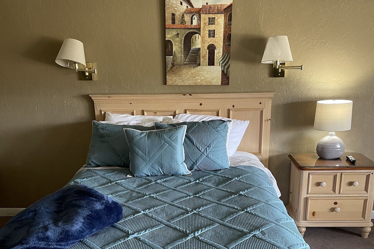 A bedroom with a bed, two wall-mounted lamps, a nightstand, and a painting on the wall.