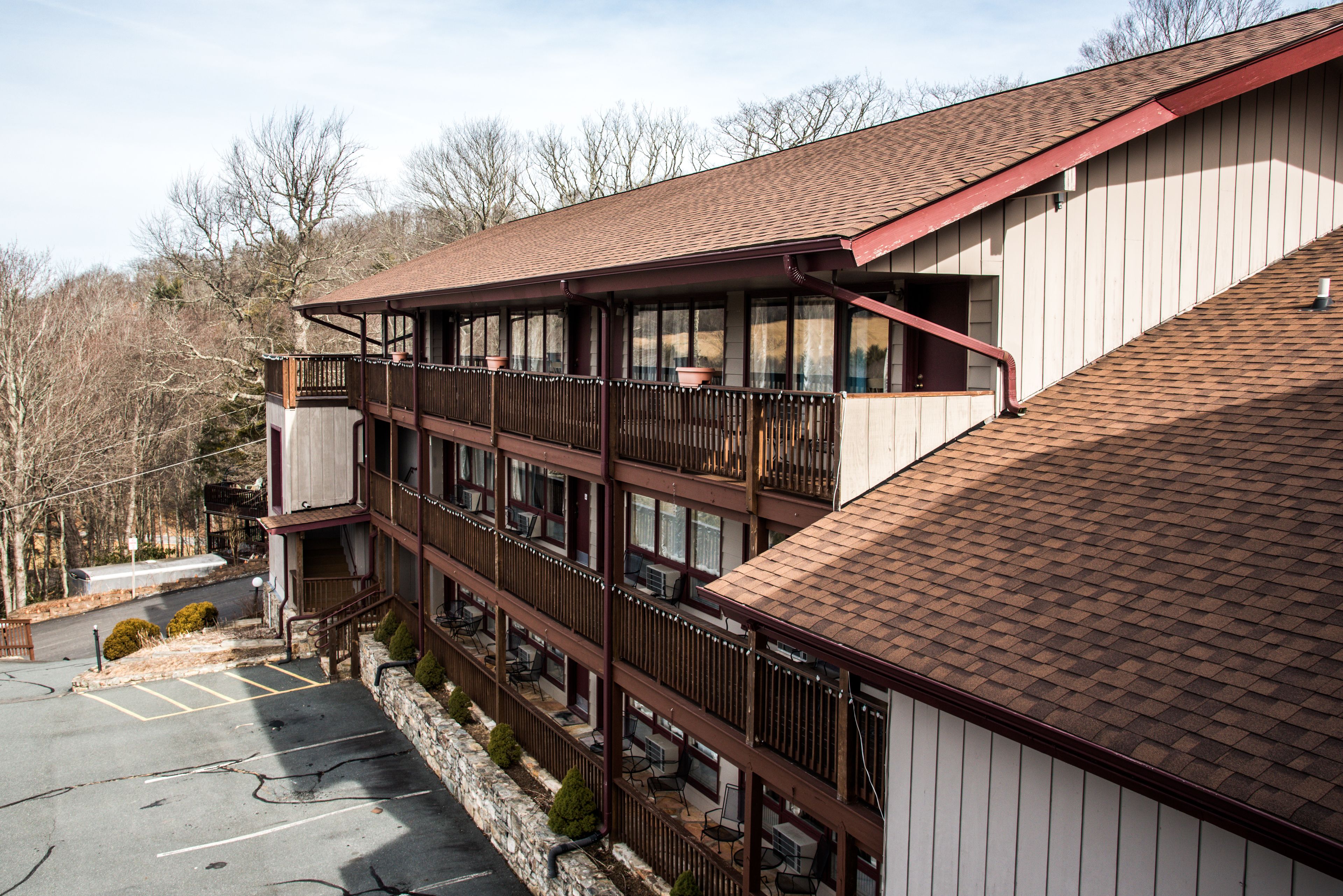 A multi-story hotel with balconies, a parking lot, and a view of trees.