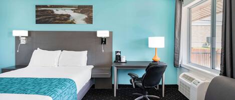 Quarto de hotel com cama, escrivaninha, cadeira e uma grande janela.
