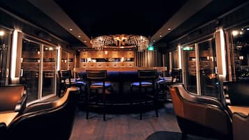 A dimly lit bar area with a central bar counter, multiple seating arrangements, and a decorative chandelier.