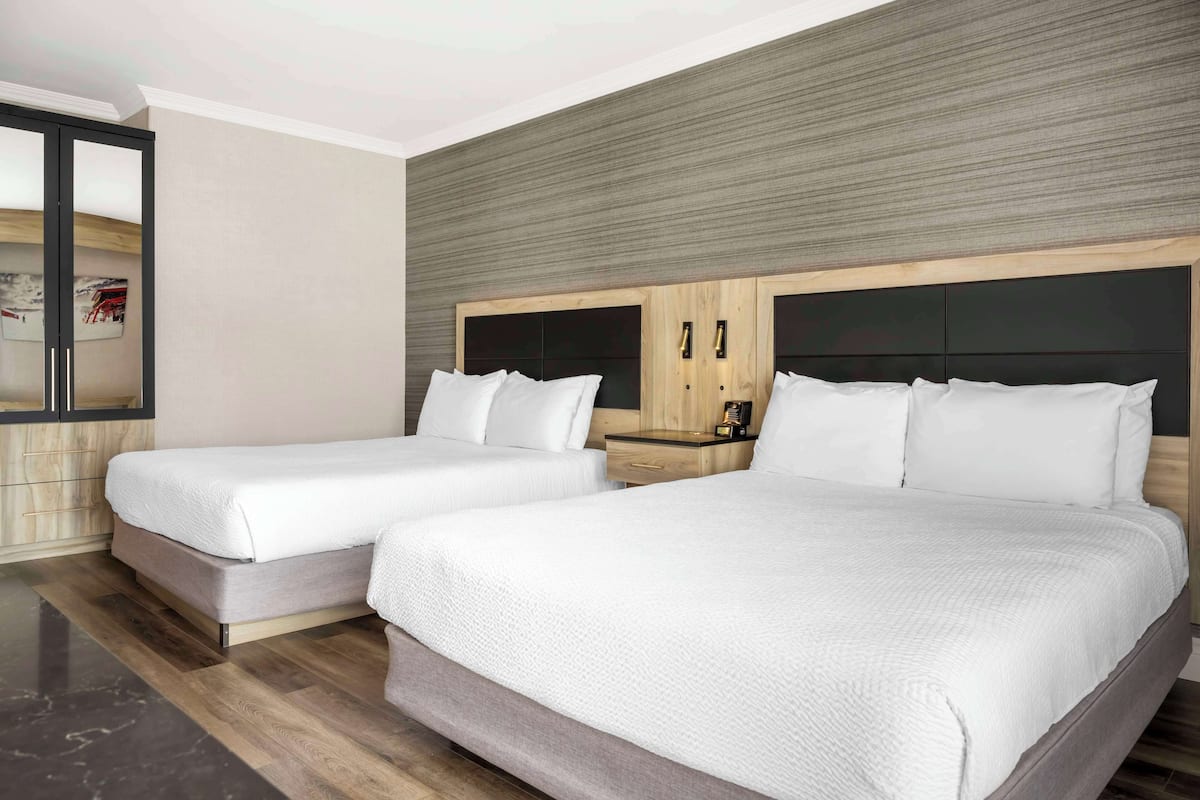 Une chambre d’hôtel avec deux lits, une armoire en bois, une table de chevet avec une lampe et un grand miroir.