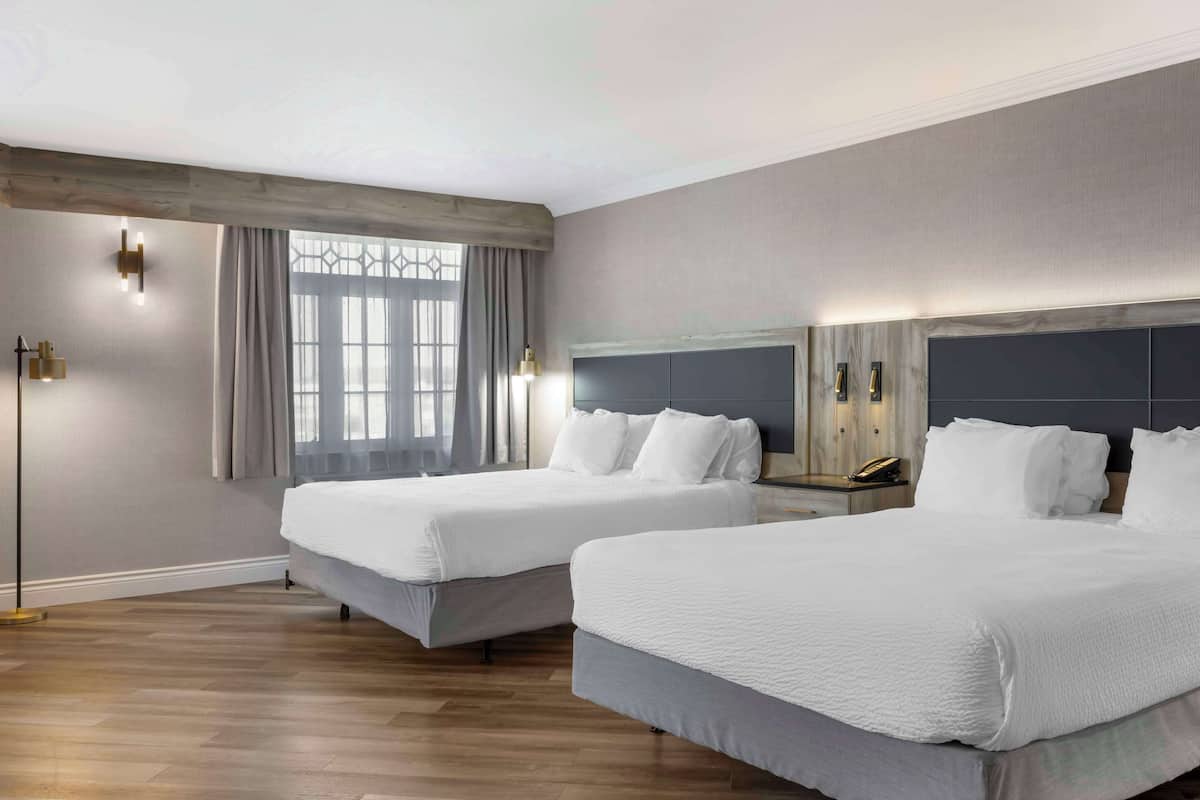 Une chambre d’hôtel avec deux lits, une grande fenêtre avec des rideaux, un luminaire moderne et un plancher en bois.
