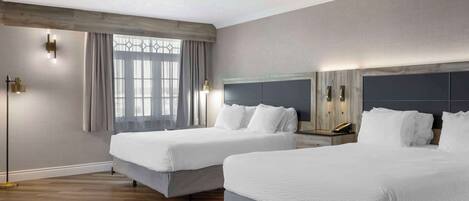 A hotel room with two beds, a large window with curtains, a modern light fixture, and a wooden floor.