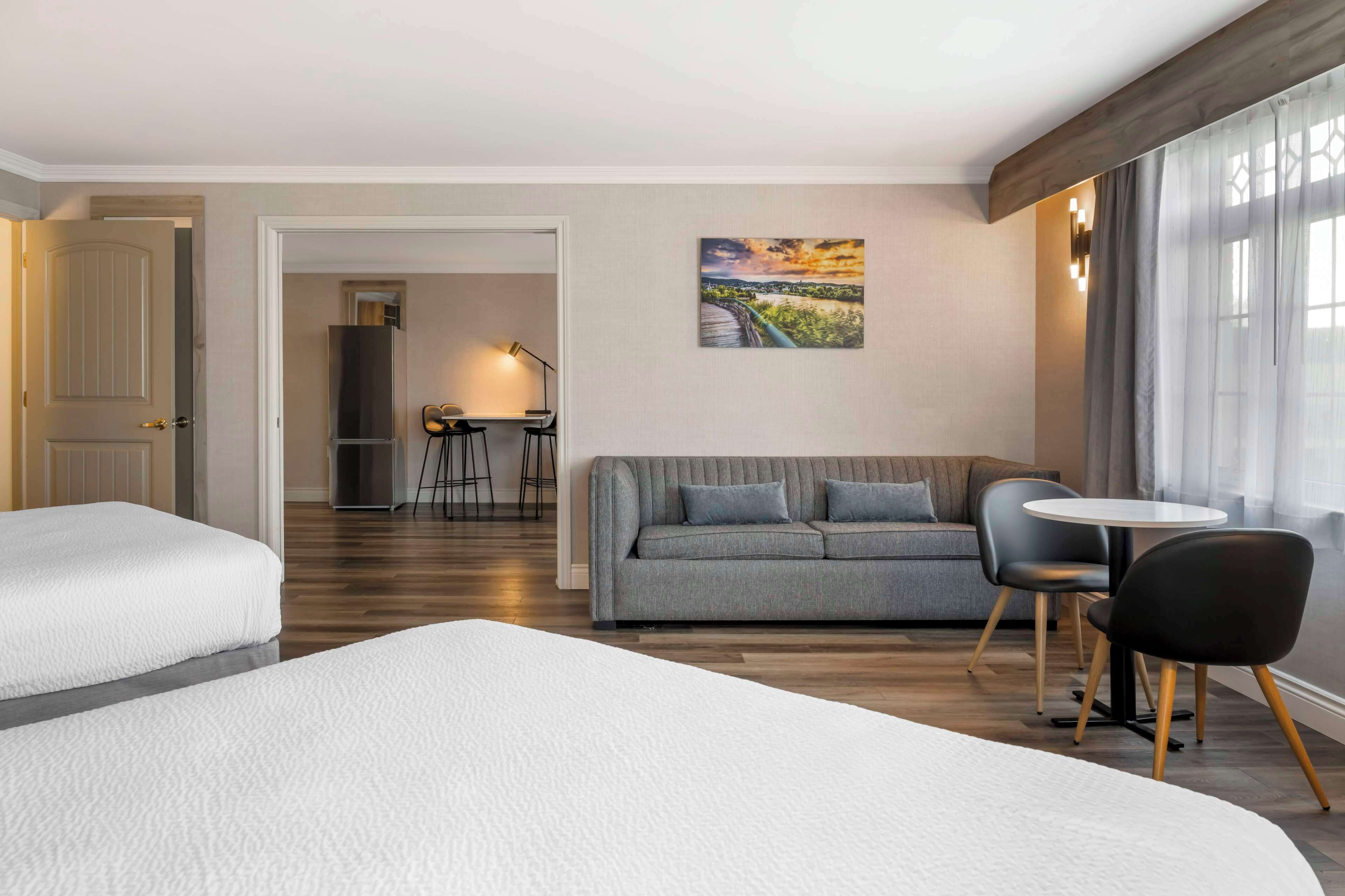 Une chambre d’hôtel avec deux lits, un canapé, une table à manger avec des chaises et un tableau au mur.