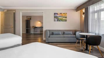Une chambre d’hôtel avec deux lits, un canapé, une table à manger avec des chaises et un tableau au mur.