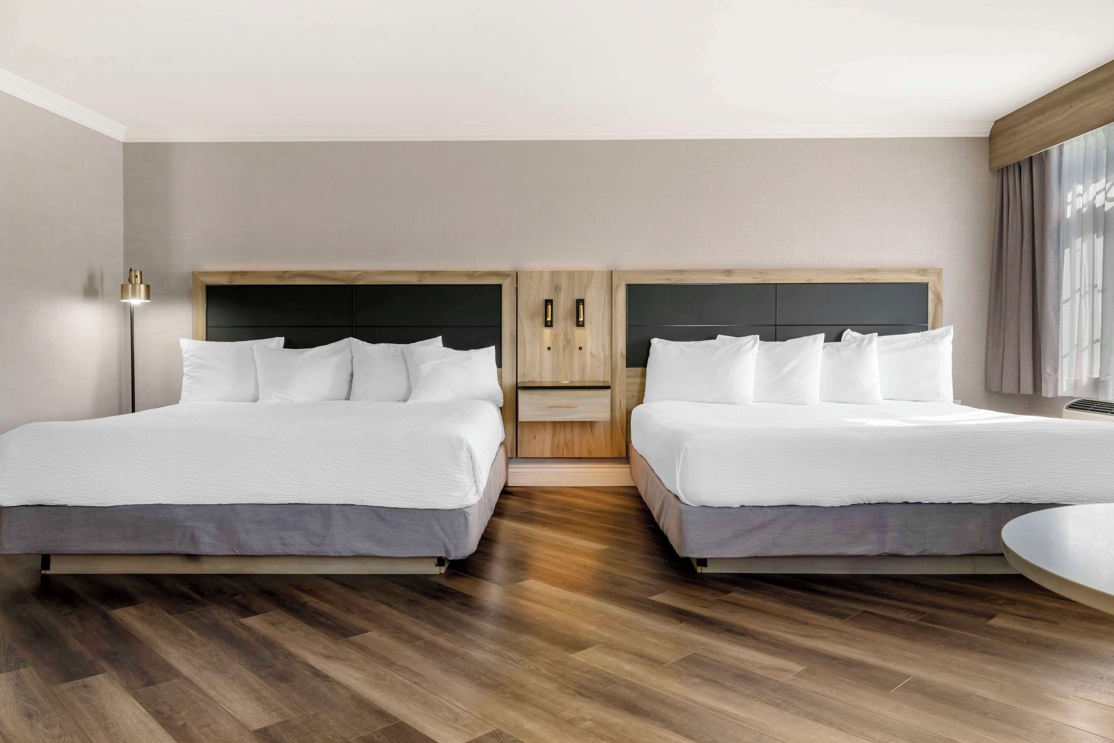 A hotel room with two beds, a wooden headboard, a bedside table, and a floor lamp.