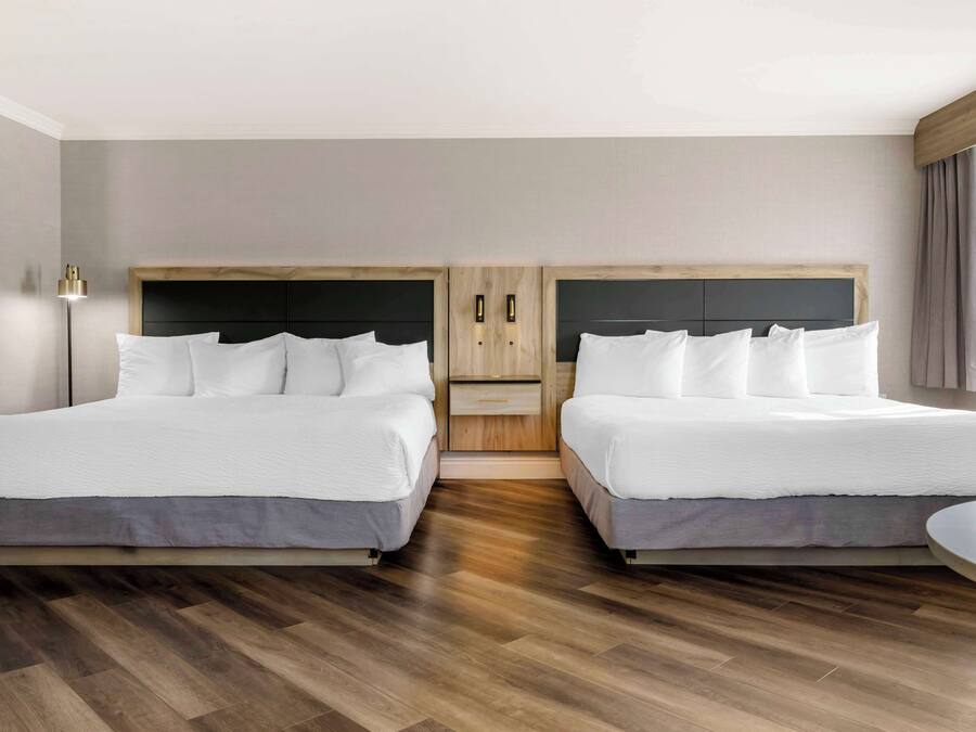 A hotel room with two beds, a wooden headboard, a bedside table, and a floor lamp.