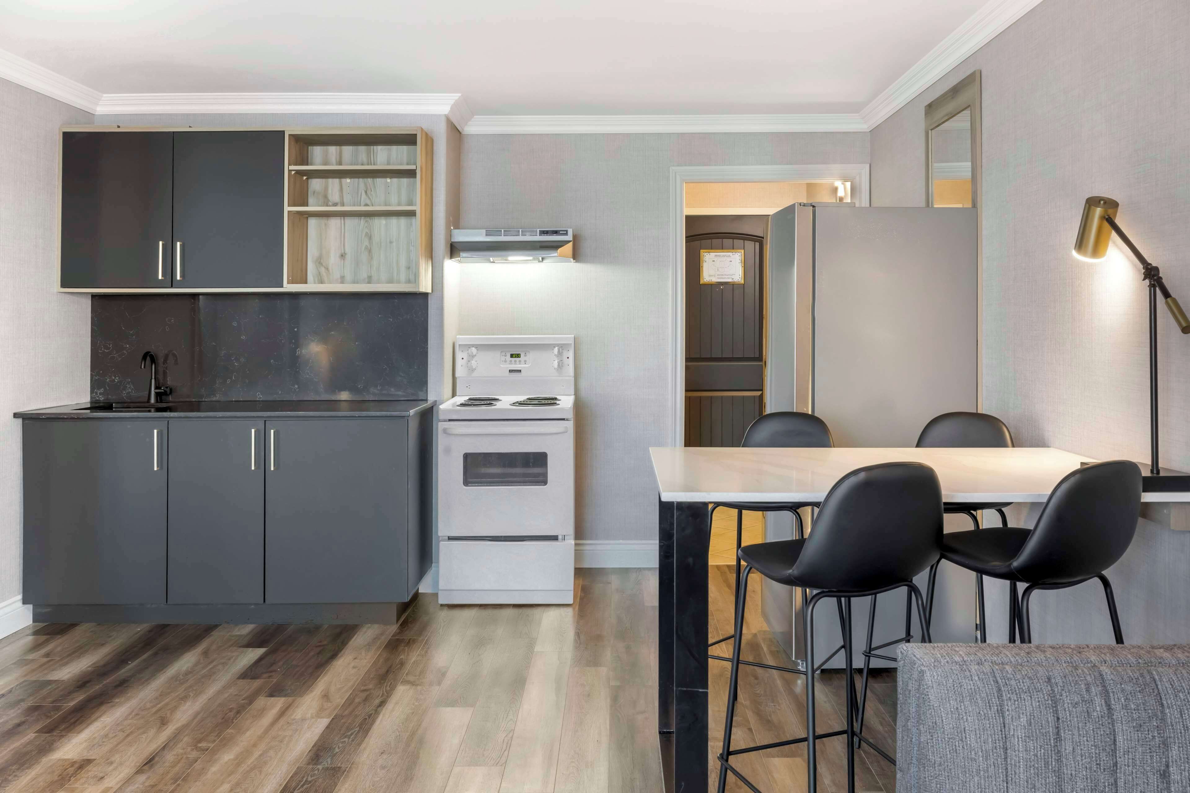A modern kitchen with dark cabinets, a white stove, and a dining area with a table and black chairs.