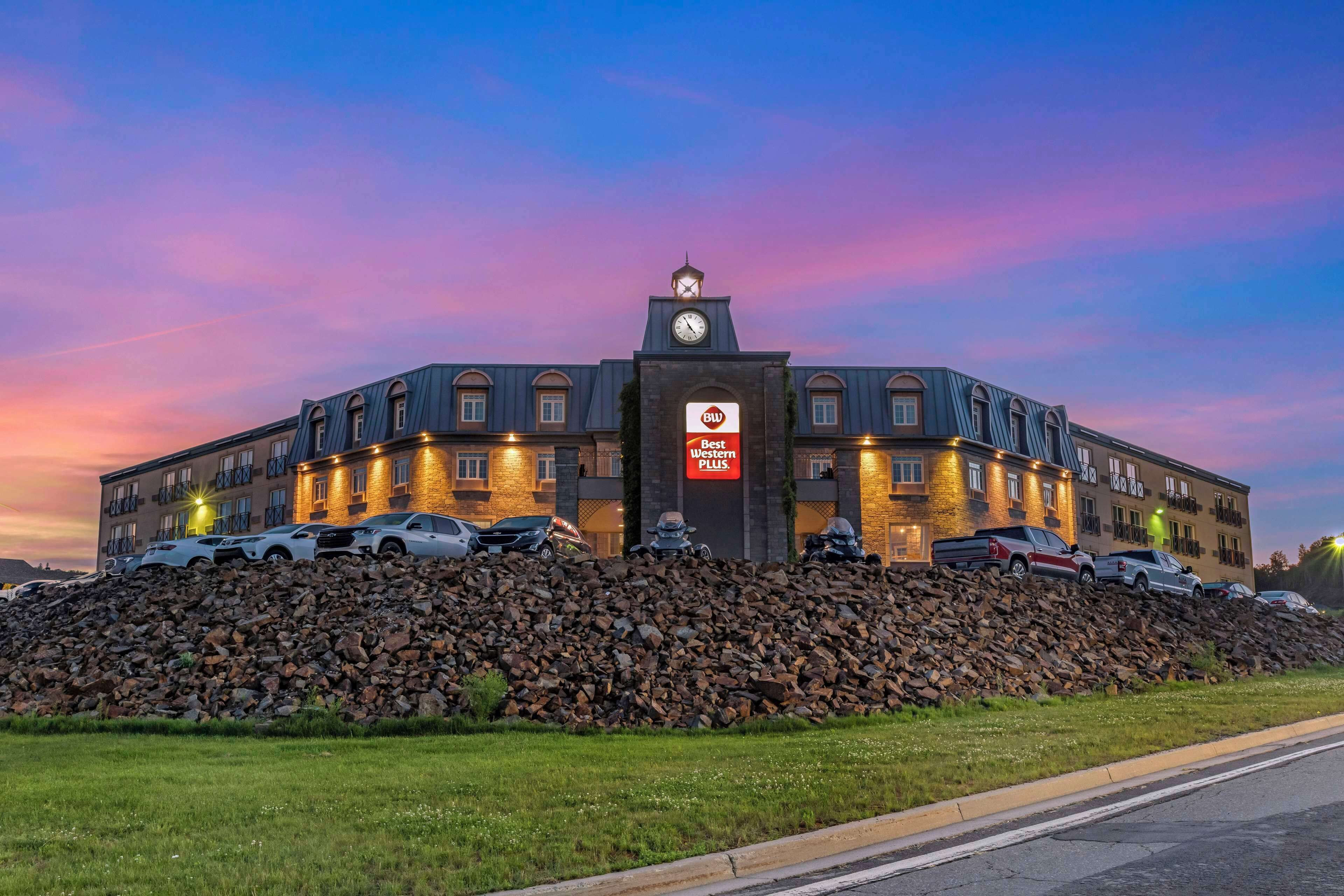 A hotel with a clock tower, a sign reading "Best Western Plus", and a parking lot with several cars.