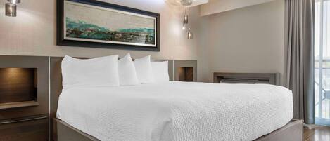 Una habitación de hotel moderna con una cama grande, una obra de arte enmarcada sobre la cama y vistas al exterior a través de la ventana.