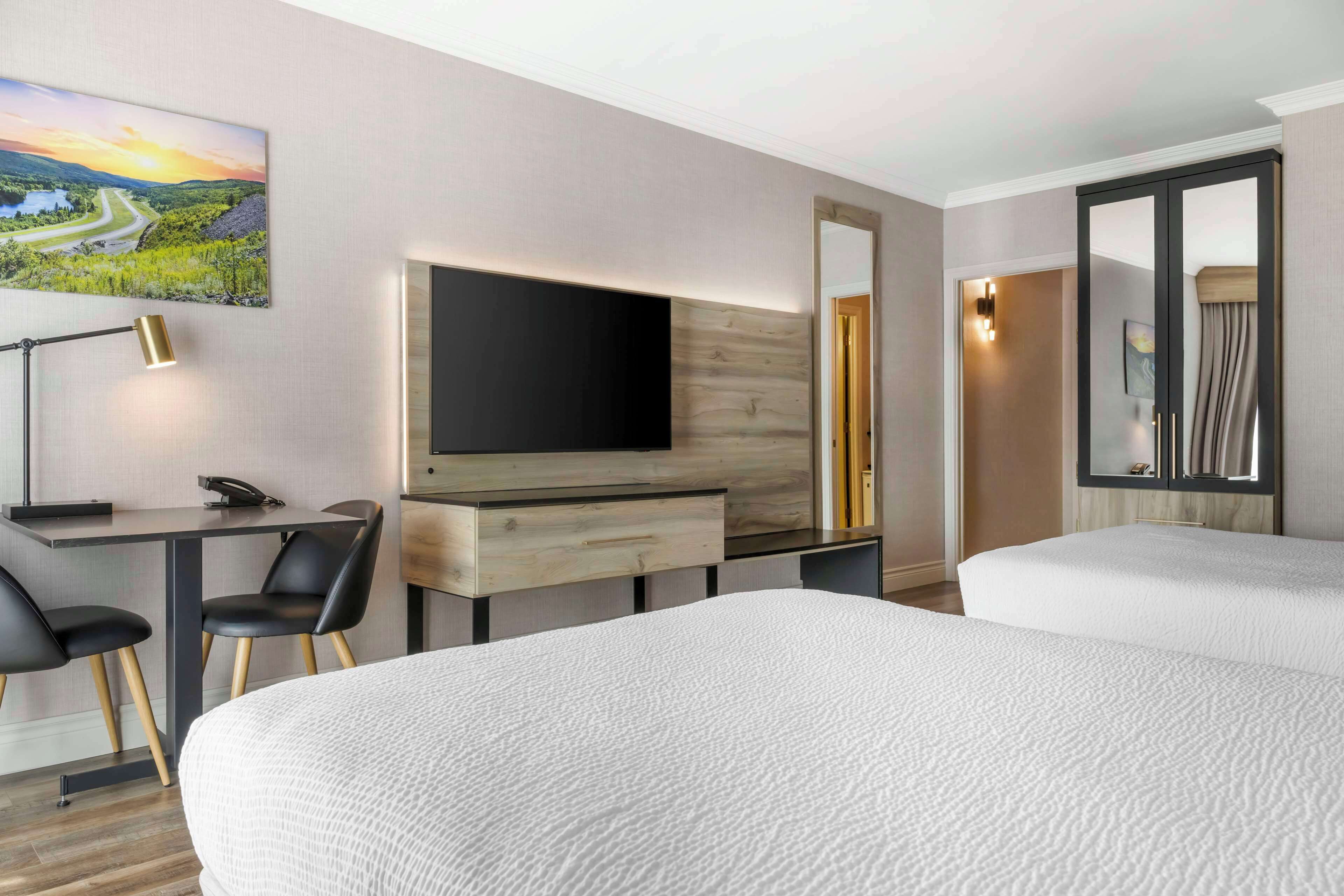 Una habitación de hotel con una cama, un escritorio con silla, un televisor y un espejo grande.