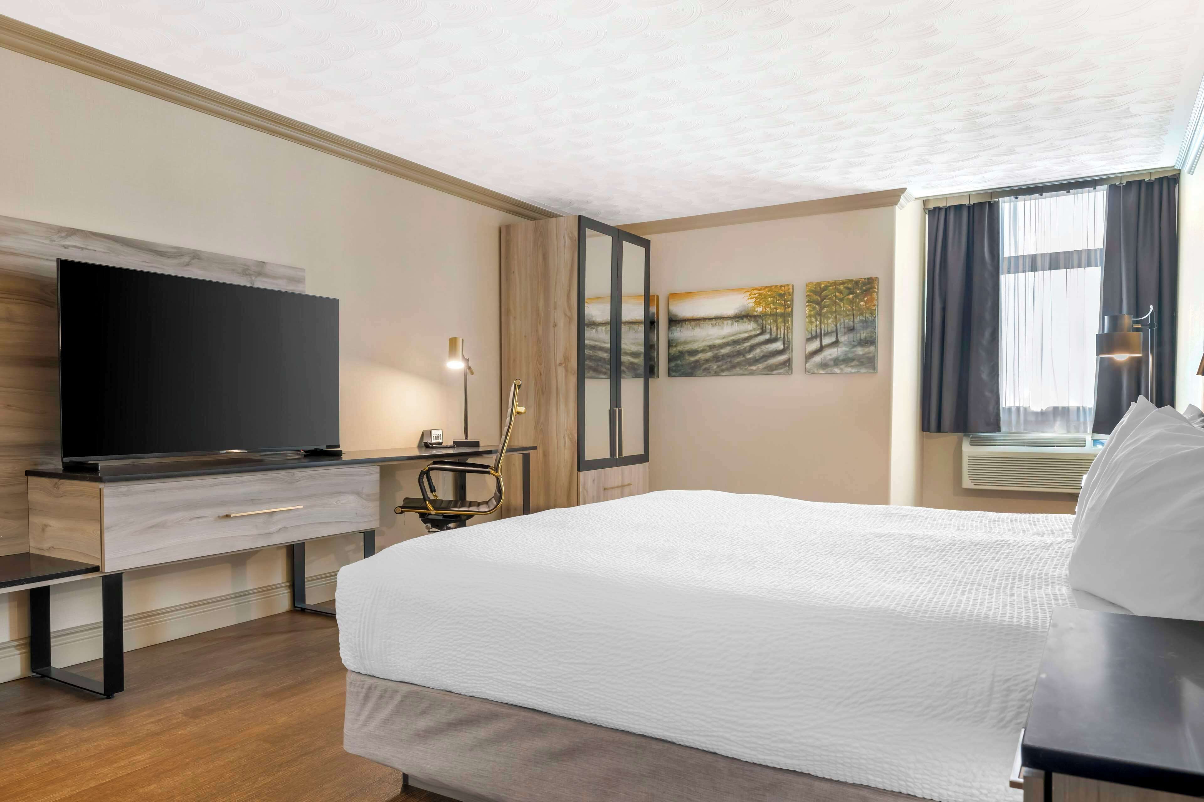 Habitación de hotel con una cama grande, un televisor de pantalla plana, un escritorio con silla y obras de arte en las paredes.