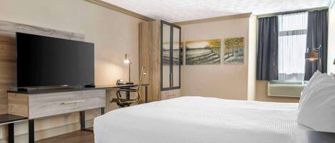 Habitación de hotel con una cama grande, un televisor de pantalla plana, un escritorio con silla y obras de arte en las paredes.