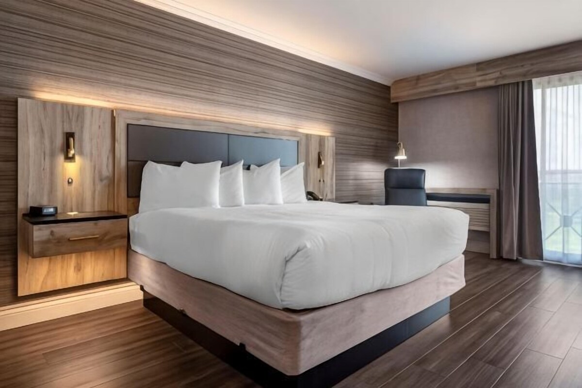 A modern hotel room with a large bed, built-in nightstands, and a view of the city.