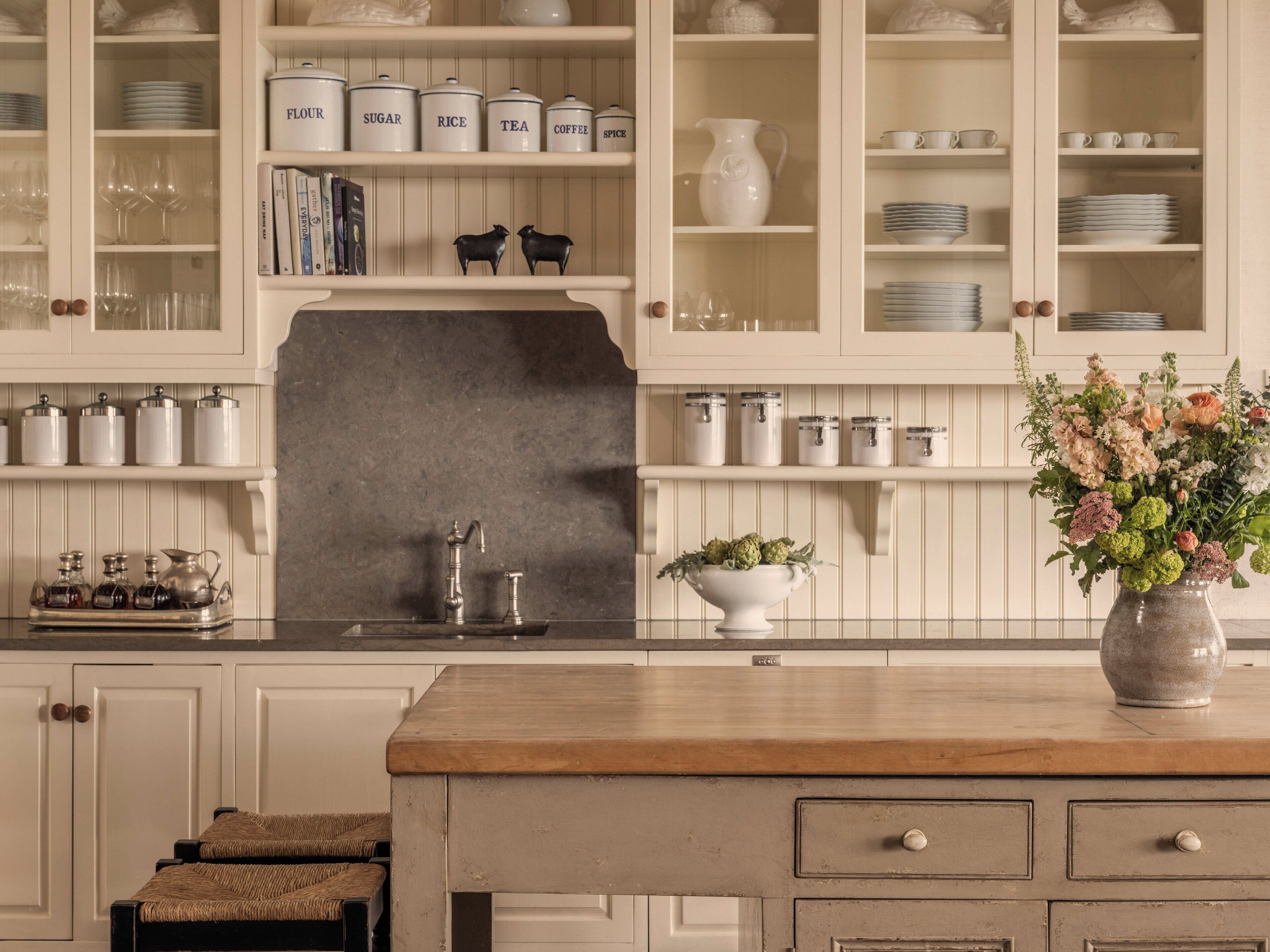 A kitchen with white cabinetry, a wooden countertop, and a vase with flowers.
