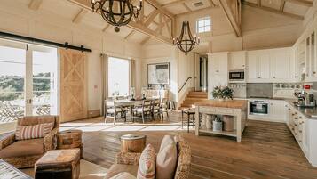 Amplia sala de estar con una mesa de comedor, una cocina con armarios blancos y un gran ventanal con vistas panorámicas.