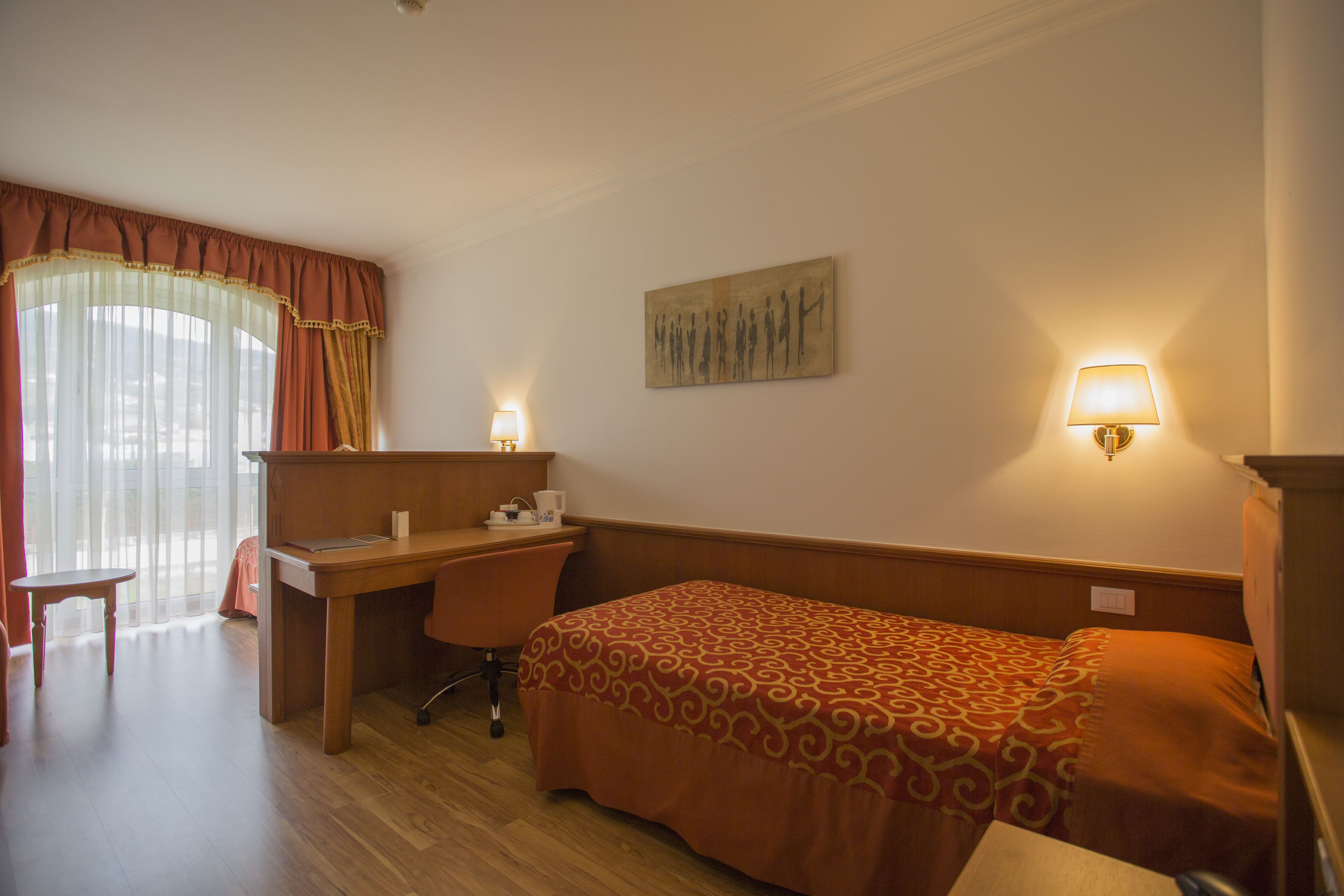 A hotel room with a bed, a desk, a chair, and two wall-mounted lamps.