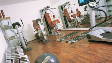 Un gimnasio con equipo de ejercicio, cinta de correr y una pantalla de televisión.