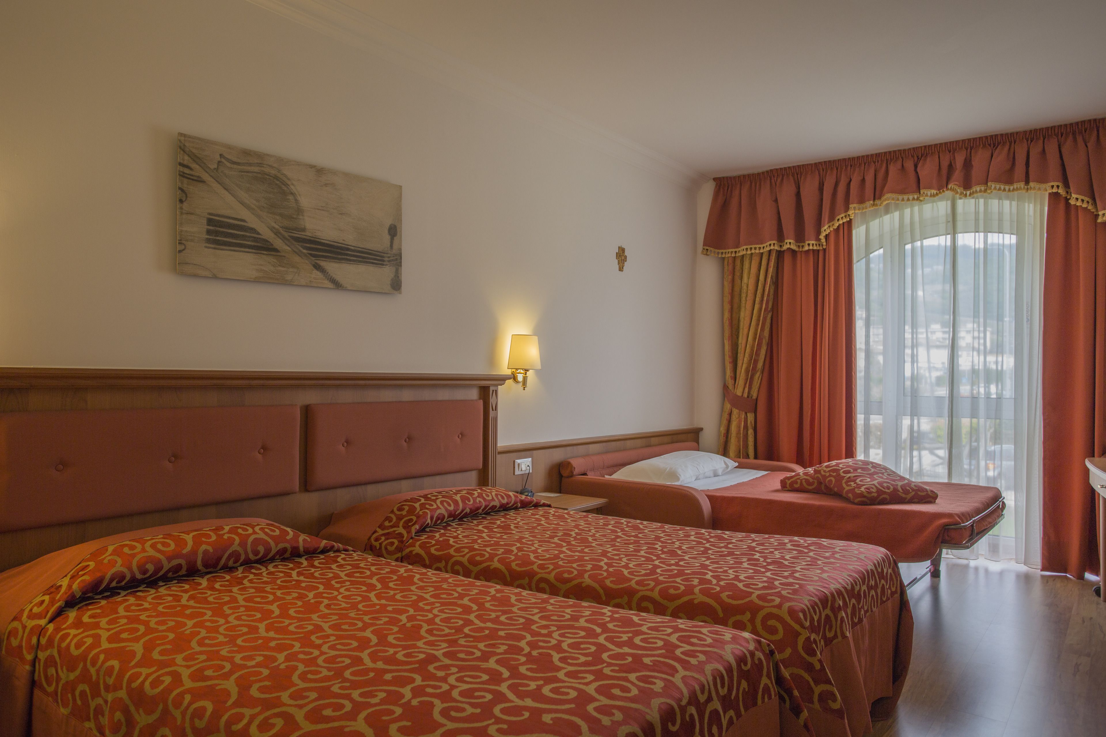A hotel room with two beds, a small table, and a window with curtains.