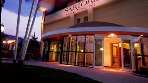 L’entrée d’un hôtel, avec une enseigne indiquant «
HÔTEL SARTORI
» et une façade en verre.