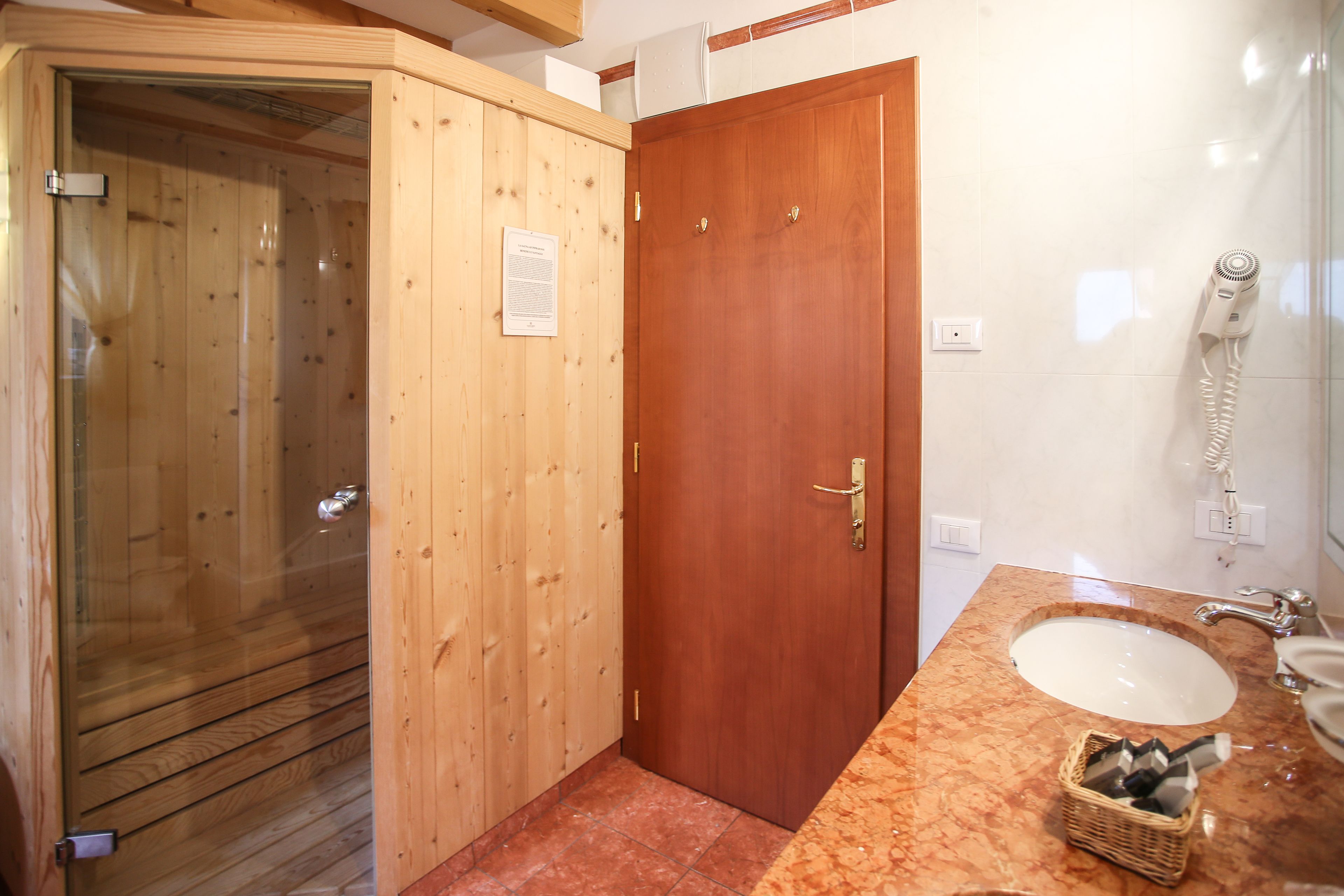 Un baño con cabina de ducha de madera, puerta de madera, lavabo de mármol y secador de pelo en la pared.