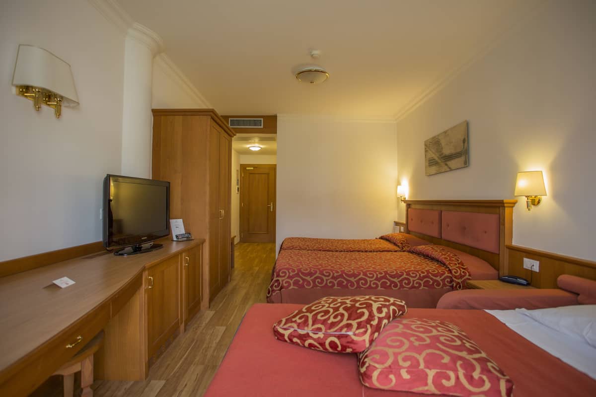 A hotel room with two beds, a desk, a television, and a lamp.