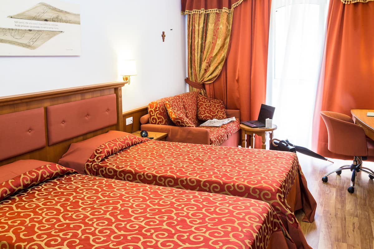 A hotel room with two beds, a desk, a chair, and a laptop.