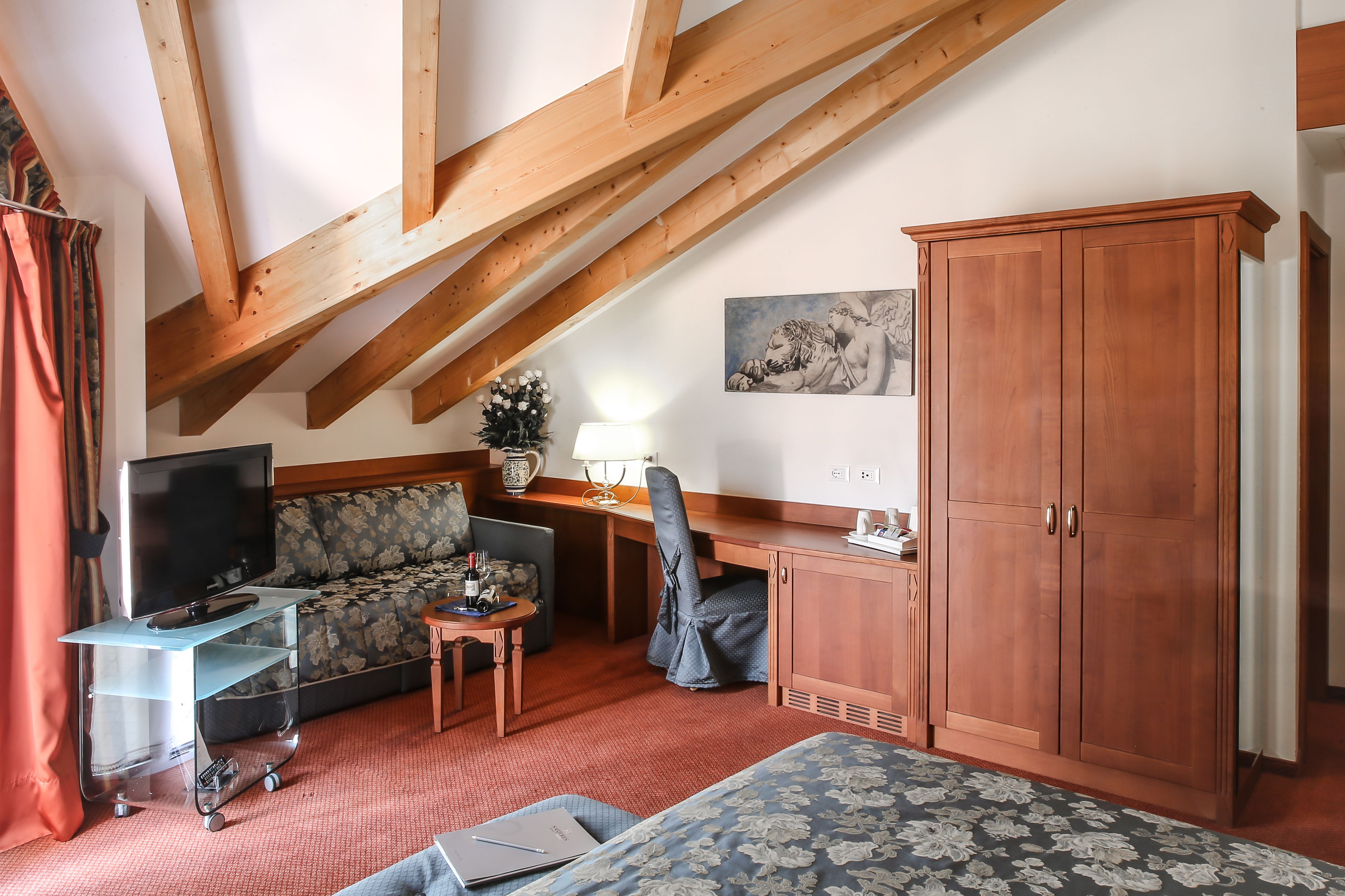 Ein Hotelzimmer mit hohen Decken, einem Sofa, einem Schreibtisch, einem Fernseher, einem Schrank und einem Bett.