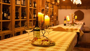 Un restaurant avec des étagères en bois remplies de bouteilles, une table recouverte d’une nappe à carreaux, des bougies et des verres à vin.