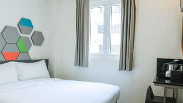 Habitación de hotel con cama, escritorio con cafetera, ventana con cortinas y un adorno geométrico en la pared.