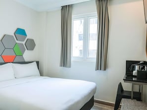A hotel room with a bed, a desk with a coffee maker, a window with curtains, and a geometric wall decoration. - ibis budget Singapore Jasmine (Singapore)