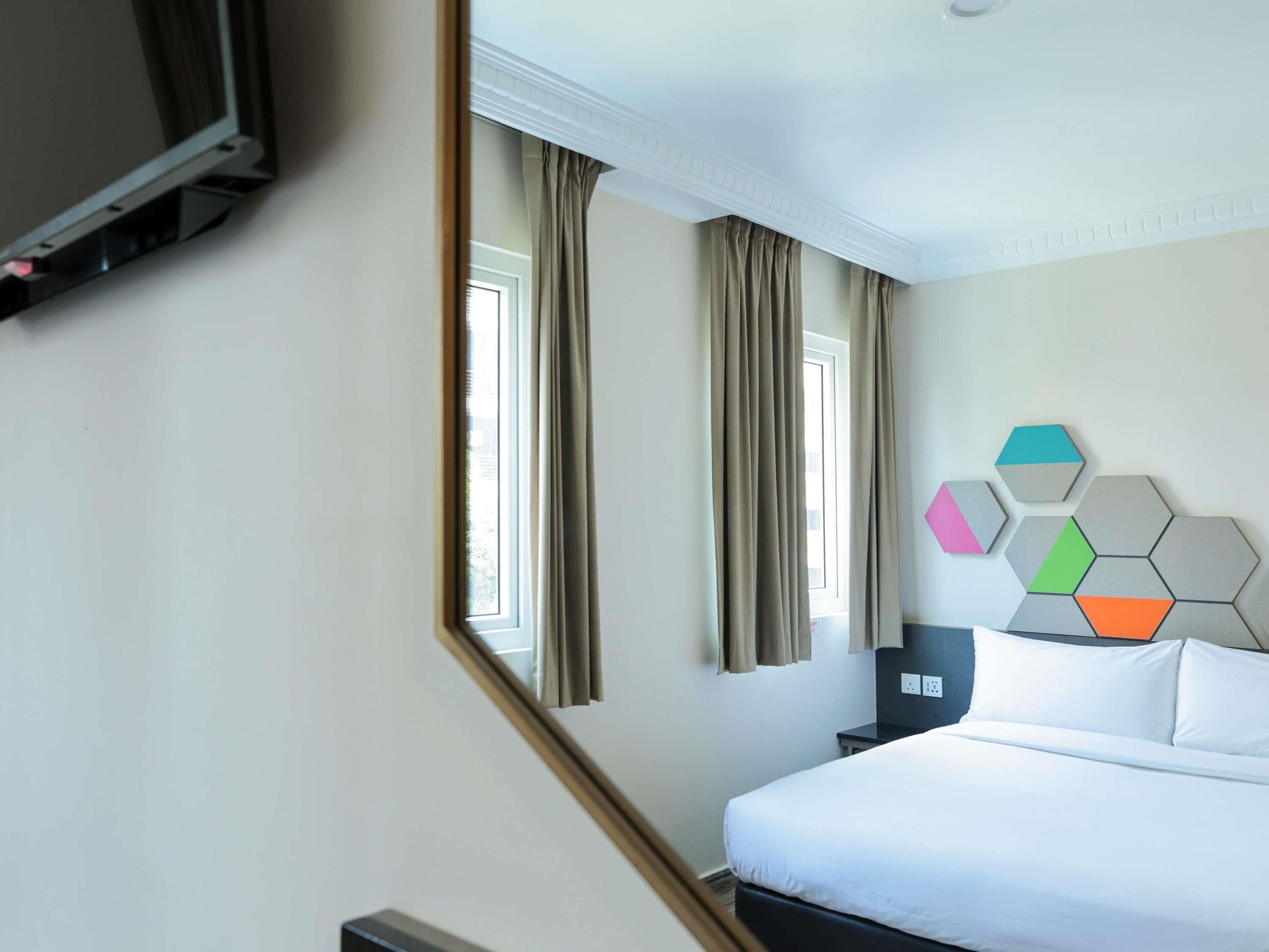 A hotel room with a bed, a nightstand, a TV, and a window with curtains.