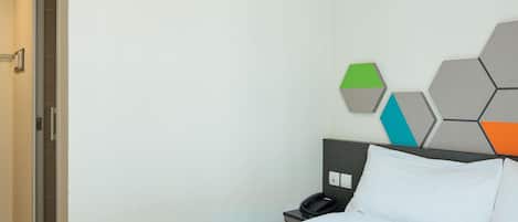 A hotel room with a bed, a nightstand with a phone, and a wall with geometric wall art.