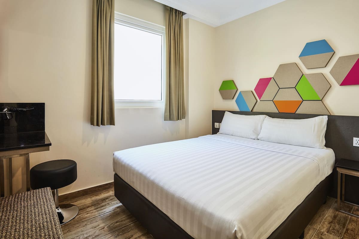 A hotel room with a bed, a desk, a chair, and a window with curtains.