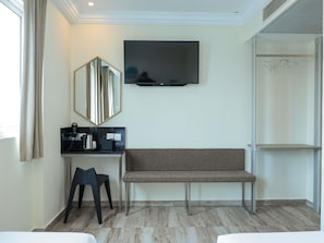 Una habitación de hotel con cama, escritorio, silla, televisor, espejo y armario.