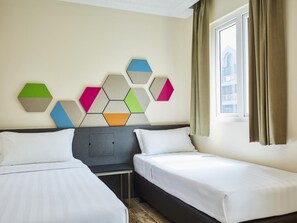Een hotelkamer met twee bedden, een geometrisch wanddecor, een raam met gordijnen en uitzicht op een gebouw.