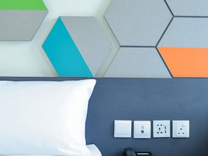 A bed with a white pillow, a grey headboard, and four electrical outlets on the wall.
